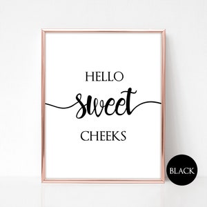 Puede incluir: Una impresión de arte de pared imprimible en blanco y negro con el texto "Hello Sweet Cheeks" en una fuente cursiva. La impresión está enmarcada en un marco de color oro rosa.