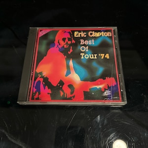 May include: A CD case with a colorful image of Eric Clapton playing a guitar. The text on the case reads "Eric Clapton Best Of Tour '74".