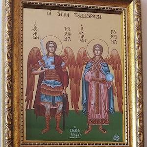 May include: A framed religious icon depicting two angels with wings, one holding a sword and the other holding a sphere. The icon is in a gold frame with ornate details. The text on the icon reads "οἱ ἅγιοι Ταξιάρχαι" and "IM.KO 47746!"
