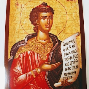 May include: An icon of Saint Paul, a religious figure, depicted in a traditional Byzantine style. He is wearing a red robe and holding a scroll with Greek text that reads "ἀγάπησε, ὁ Θεὸς οὖ, Παῦλος βασι, λεῖται ἦτε, εἰς ἐαῖτος, ἦας οὖ, ἀφοραη, σεται."
