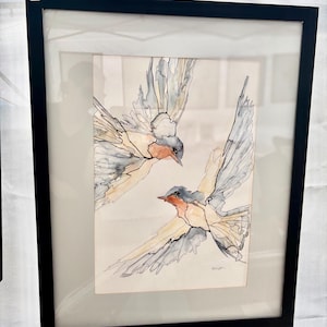 K&ouml;nnte beinhalten: Ein gerahmtes Aquarellbild, das zwei fliegende Schwalben zeigt. Die V&ouml;gel sind mit sanften Waschungen in Blau-, Grau- und Pfirsicht&ouml;nen dargestellt, die durch feine schwarze Tintenumrisse definiert sind. Das Kunstwerk ist in einem schwarzen Rahmen.