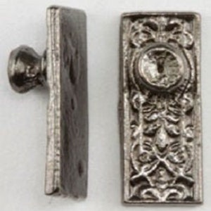 May include: Two antique silver-toned drawer pulls. One pull features a small knob, the other has an ornate rectangular design with a central jewel and floral details. The pulls are likely made of metal.
