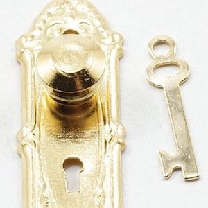 May include: A gold-colored, ornate door handle with a matching key. The door handle has a round knob and a decorative backplate with intricate detailing. The key is a simple, classic design. The items are likely for a dollhouse or miniature project.