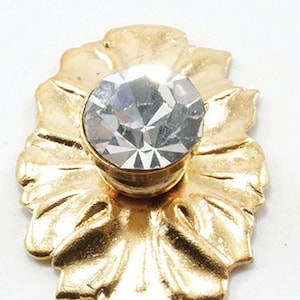 Puede incluir: Un pomo decorativo de metal dorado con un centro de cristal transparente. El pomo tiene un diseño floral.