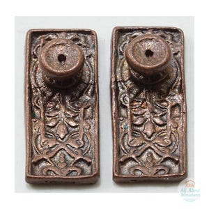 May include: Two rectangular copper-toned drawer pulls featuring an intricate embossed floral and vine pattern. Each pull has a central circular knob with a small hole in the middle. The metal surface has a weathered, textured finish.