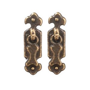 May include: Two vertical antique brass drawer pulls featuring a rectangular backplate with decorative scalloped ends and a central swinging ring handle. The metal hardware has a dark, weathered finish with highlighted edges and a smooth texture.