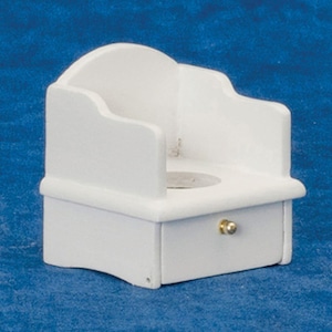 May include: A miniature white wooden chair featuring a rounded backrest, curved armrests, and a single front drawer equipped with a small, round, gold-colored metal knob. The seat of the chair contains a circular cutout in the center.