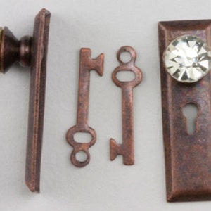 May include: A set of antique-style door hardware in a copper finish. The set includes a door knob with a crystal-like knob, a keyhole cover, and two skeleton keys.
