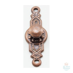 May include: A copper-toned metal drawer pull featuring a central circular knob mounted on an elongated, decorative backplate with floral-inspired details and two screw holes at the top and bottom. The text AAM All About Miniatures is visible.