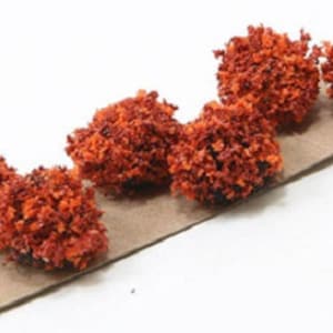 May include: Five small, orange, fluffy, round, decorative bushes. The bushes are arranged in a row on a brown paper card.