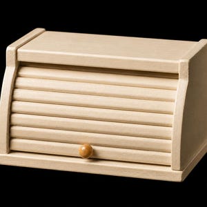 May include: A miniature wooden bread box with a roll-top design. The box is painted in a light beige color and features a small wooden knob for opening. The roll-top is made of horizontal wooden slats. The bread box is a charming addition to a dollhouse or miniature collection.