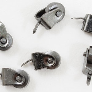 May include: Six silver-toned metal furniture casters with wheels. The casters have a small metal pin protruding from the side.