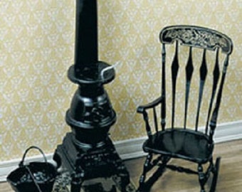 May include: Miniature black stove with a chimney, a rocking chair, a small stool, a bucket, and a shovel. The stove sits on a decorative mat. The rocking chair has a detailed back. The scene is set against a patterned wallpaper.