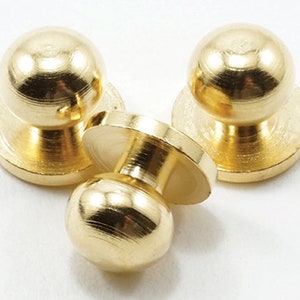 Puede incluir: Tres pomos de metal de color dorado con parte superior redonda y base plana. Los pomos tienen un acabado liso y pulido.