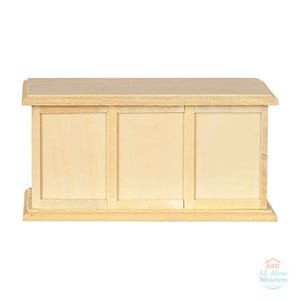 May include: A miniature wooden desk with a light tan finish, featuring a rectangular top and a front panel divided into three vertical sections. The piece includes the text AAM All About Miniatures in the bottom right corner.