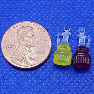 Puede incluir: Dos botellas de vidrio en miniatura con tapones. La botella de la izquierda está llena de un líquido amarillo y la botella de la derecha está llena de un líquido morado. Las botellas están sobre una superficie azul.