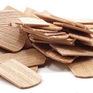 Op de afbeelding: Een stapel kleine, rechthoekige houten stukjes met afgeronde randen. Het hout heeft een lichtbruine kleur en een zichtbaar nerfpatroon. De stukjes zijn verspreid, wat suggereert dat ze los of niet bevestigd zijn.