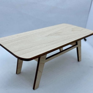May include: A small wooden table with a light wood finish and a simple design. The table has a rectangular top and four legs.
