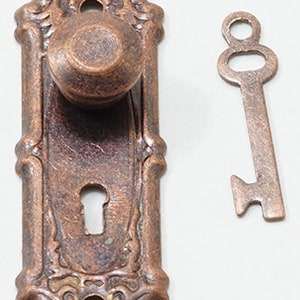 Pode incluir: Uma maçaneta de porta e uma placa de fechadura de estilo vintage com um design decorativo. A maçaneta e a placa são feitas de metal e têm um acabamento em cobre. A chave também é feita de metal e tem um acabamento em cobre.