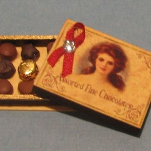 May include: Miniature box of assorted fine chocolates, with a red ribbon and a vintage illustration on the lid. The box contains several chocolate pieces, including one wrapped in gold foil.