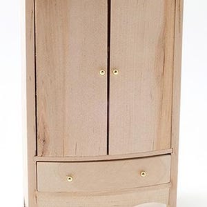 May include: A miniature wooden armoire with two doors and a drawer. The armoire is made of light-colored wood and features brass-colored knobs. The drawer has a curved bottom edge. The armoire is designed for a dollhouse or miniature setting.