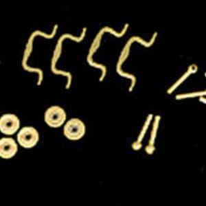 May include: A collection of gold-toned jewelry findings including several wavy wire components, a group of small circular washers or spacers, and a set of straight pins with small circular loops at one end, all arranged on a dark background.