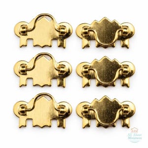 Pode incluir: Seis puxadores de gaveta de metal dourado dispostos em duas colunas de três. Cada puxador apresenta uma placa decorativa em forma de escudo com uma alça articulada. O texto All About Miniatures é visível no canto inferior direito.
