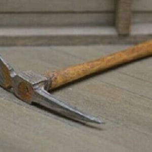 May include: A small, wooden-handled pickaxe with a metal head. The pickaxe is made of metal and wood and has a brown wooden handle.
