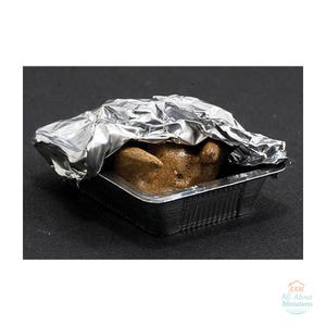 Może przedstawiać: Miniaturowy pieczony kurczak w kwadratowej aluminiowej tacce, częściowo przykryty pogniecionym arkuszem srebrnej folii aluminiowej. Kurczak ma złocistobrązową, teksturowaną powierzchnię i znajduje się w metalowym pojemniku.