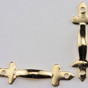 Puede incluir: Dos soportes de esquina de metal dorado con un diseño decorativo. Los soportes tienen una forma curva y un extremo puntiagudo.