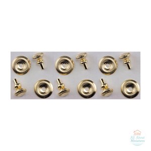Può includere: Un set di pomelli in miniatura in metallo dorato e piastre circolari abbinate con una texture a coste radiali. Ogni pomello presenta un piccolo stelo e una parte superiore arrotondata. Il testo AAM All About Miniatures è visibile in basso a destra.