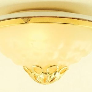 Op de afbeelding: Een close-up van een plafondlamp. De armatuur heeft een goudkleurige rand en een matglazen kap. De kap heeft een geschulpte rand en een decoratieve goudkleurige basis.