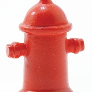 Op de afbeelding: Een kleine, felrode brandkraan met een afgeronde bovenkant en twee zijsproeiers. De brandkraan is een miniatuurreplica, waarschijnlijk een decoratief item of speelgoed, en steekt af tegen een effen witte achtergrond. De verf heeft een licht getextureerd uiterlijk.