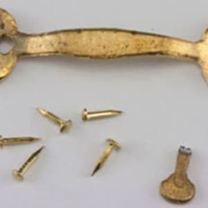 May include: A gold-toned metal handle with a textured surface and pointed ends, featuring circular mounting plates with pre-drilled holes. Included are five small gold-toned nails and a single small gold-toned metal key with a round head.