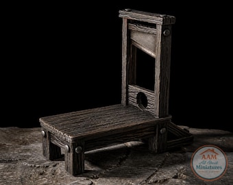 May include: A miniature wooden guillotine with a weathered, dark brown finish. The model features a blade, a neck hole, and a platform, designed to resemble the historical execution device. The miniature is set against a dark background.