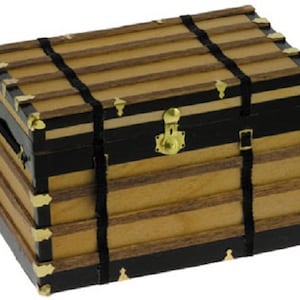 Può includere: Un baule in legno in stile vintage con cinturini in pelle nera e dettagli in ottone. Il baule ha un design a strati con una finitura in legno chiaro e dettagli neri.