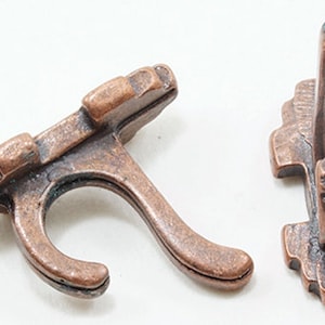 May include: Two antique copper-colored hooks with a decorative design. The hooks are made of metal and have a rustic finish.