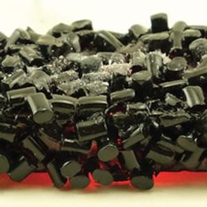 Peut inclure: Un objet décoratif rectangulaire composé de nombreuses petites pièces cylindriques noires et brillantes densément assemblées. Le centre présente un amas de fragments cristallins translucides, dentelés et clairs incrustés dans la structure.