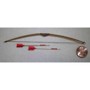 May include: A miniature wooden bow and two arrows with red fletching. The bow is brown with a dark brown leather grip. The arrows are silver with red tips. A penny is included for scale.