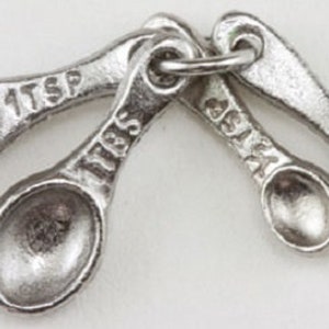 May include: Set of four silver-toned measuring spoons with a ring connecting them. The spoons are labeled "1/4 tsp", "1/2 tsp", "1 tsp", and "1/8 tsp".