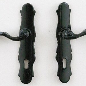 May include: A pair of black metal door handles with matching backplates. Each handle features a curved lever design attached to a vertical, elongated backplate that includes a keyhole cutout at the bottom. The finish is a solid, glossy black.