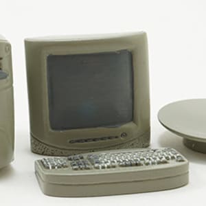 May include: A miniature computer set in a muted green color. The set includes a tower, monitor, keyboard, and a round, raised platform. The keyboard has detailed keys, and the monitor has a dark screen. The set is likely a decorative item or toy.