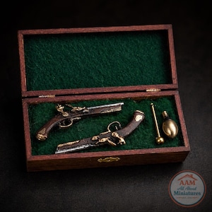 May include: Miniature replica of two antique flintlock pistols, presented in a wooden box with a green felt lining. The pistols feature intricate detailing with silver and gold accents, along with a small brass rod and flask.