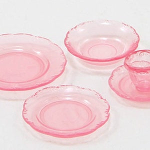 Puede incluir: Un juego de té rosa con una taza, un platillo y tres platos. El juego está hecho de vidrio y tiene un borde delicado y festoneado.