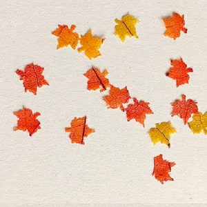 May include: Assortment of fall leaves in shades of orange and yellow. The leaves are scattered on a white surface.