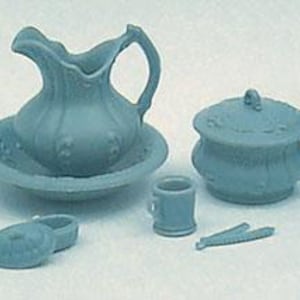 Op de afbeelding: Een verzameling miniatuur blauwe keramische badkameraccessoires. De set bevat een kan en waskom, een pot met deksel, een kleine mok, een zeepbakje en een tang. De items zijn gerangschikt op een wit oppervlak.