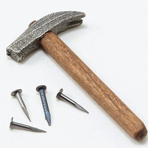 May include: A hammer with a textured, silver-colored head and a wooden handle. Four nails of varying colors and sizes are scattered near the hammer, suggesting a carpentry or construction theme.