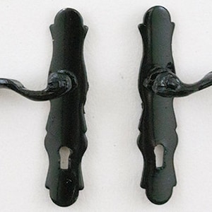 May include: Two black door handles with ornate designs and keyholes. The handles have a curved lever and a decorative plate.