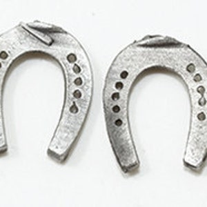May include: Four silver-coloured horseshoes with decorative holes. The horseshoes are arranged in a row, with the open ends facing each other.