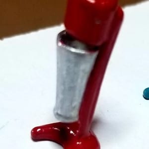 May include: A red and silver miniature milkshake maker. The base is red and the cup is silver with a textured surface.